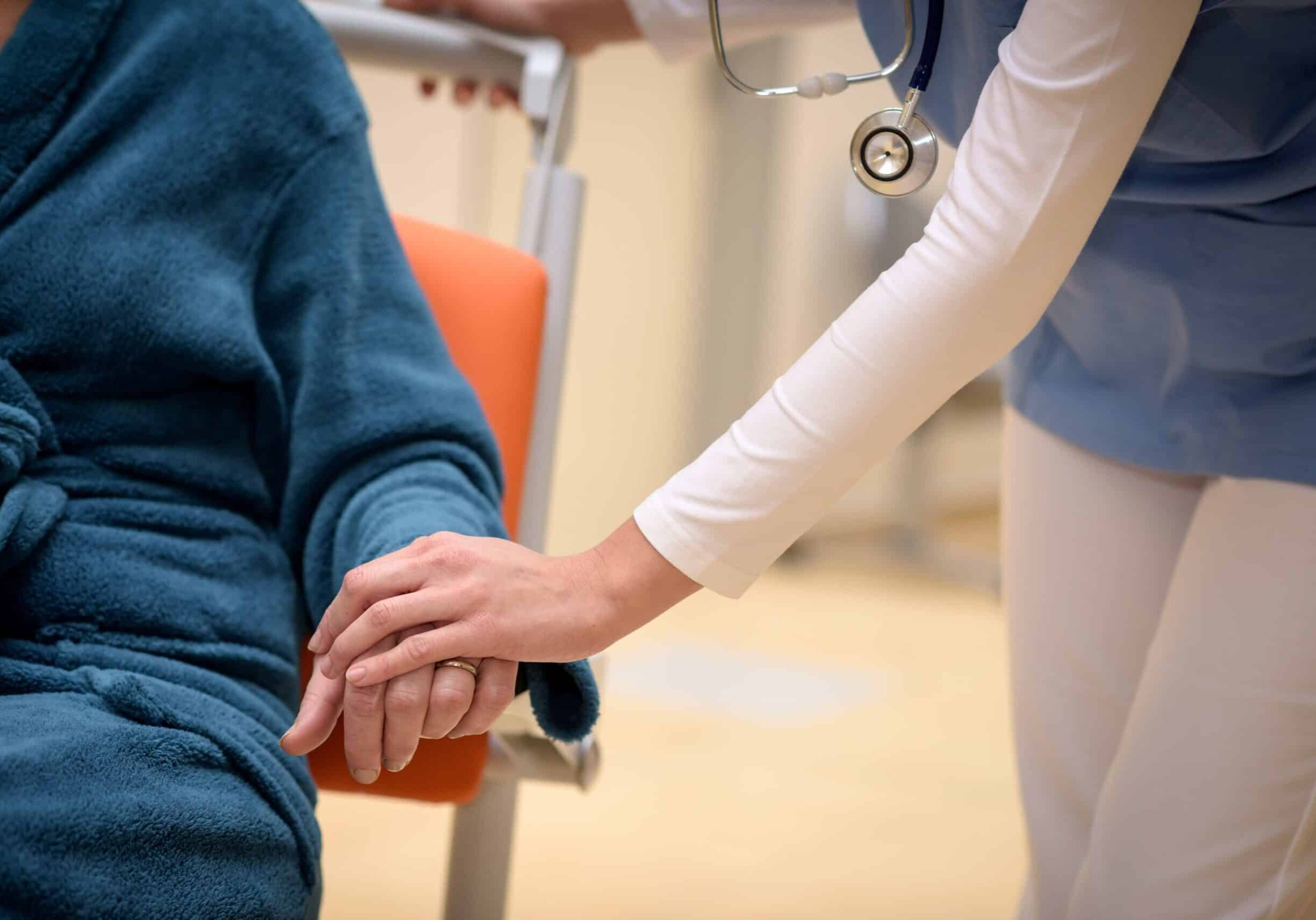 close-up-of-doctor-holding-senior-patient-hand-sitting-in-wheelchair