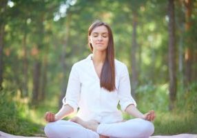 portrait-of-calm-woman-sitting-in-pose-of-lotus-in-natural-environment